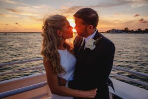 Couple in wedding attire on the bow of a boat at sunset.